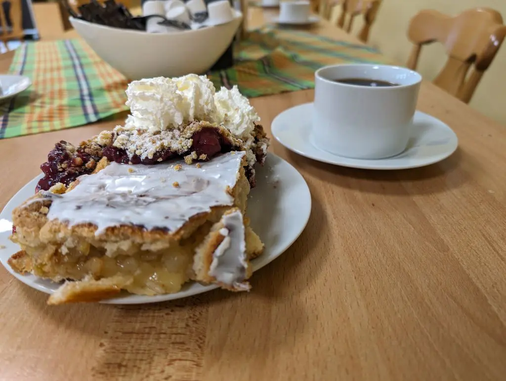 Tasse Kaffee und Teller mit Kirschstreussel und gedecktem Apfelkuchen